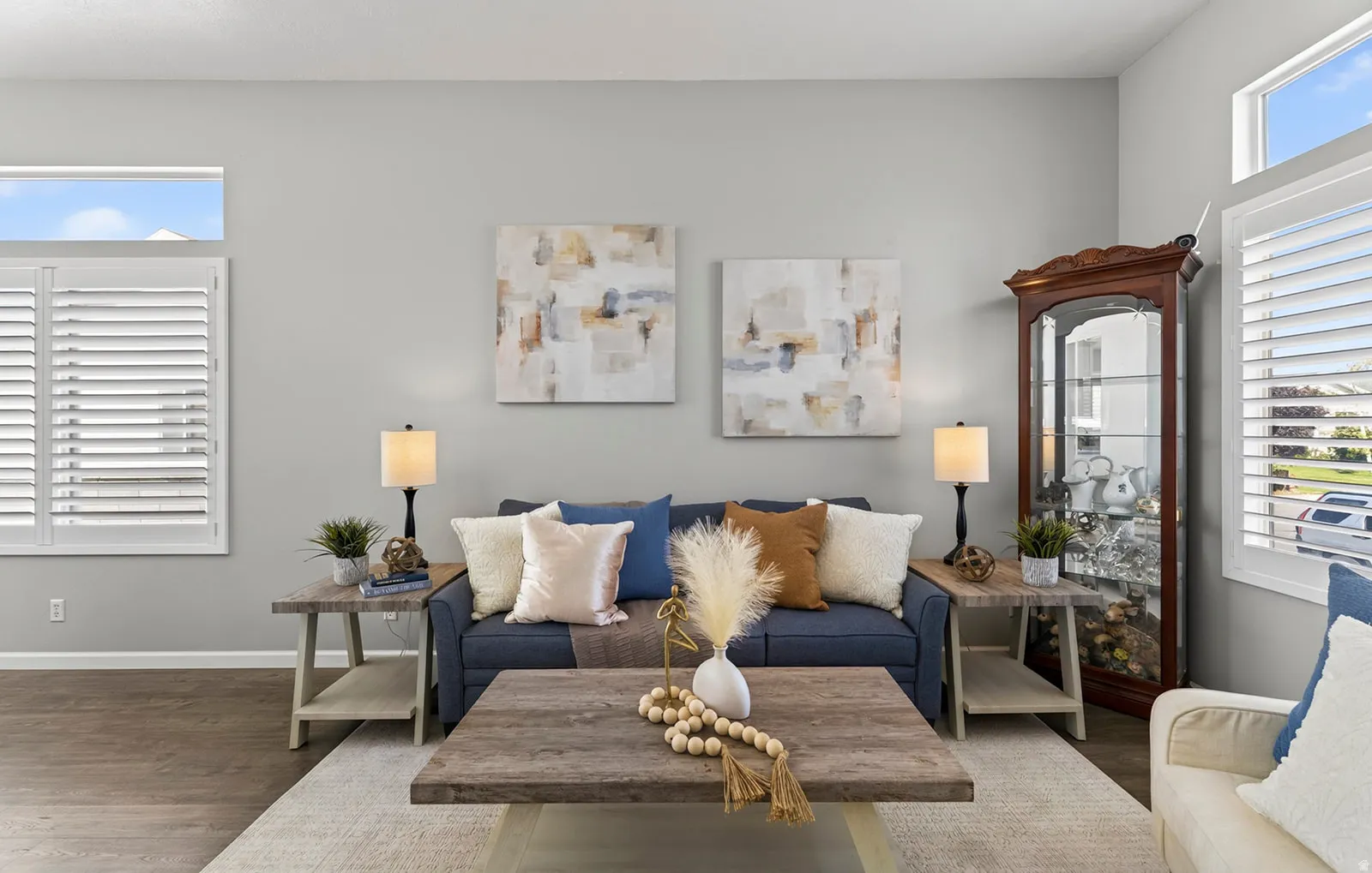 Plantation shutters on multiple windows, wood-finish flooring, light gray wall paint, and a built-in display cabinet