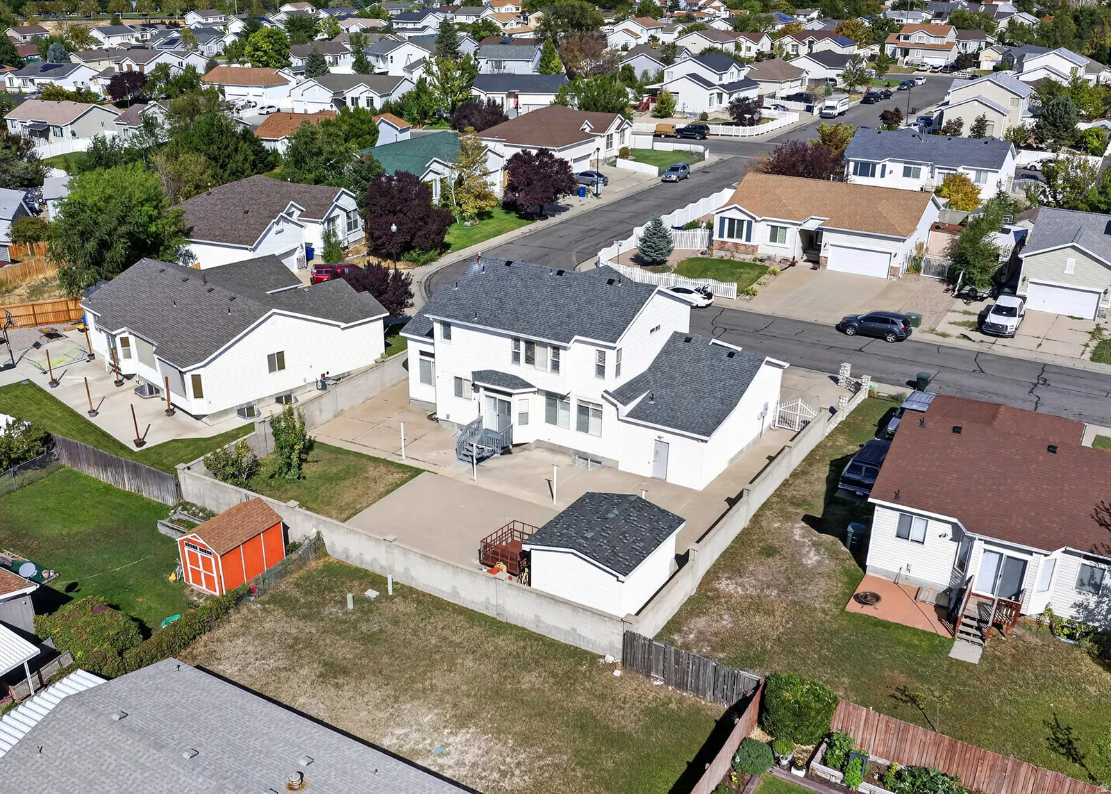 Two-story residence with a gray shingle roof, concrete patio, and a detached shed