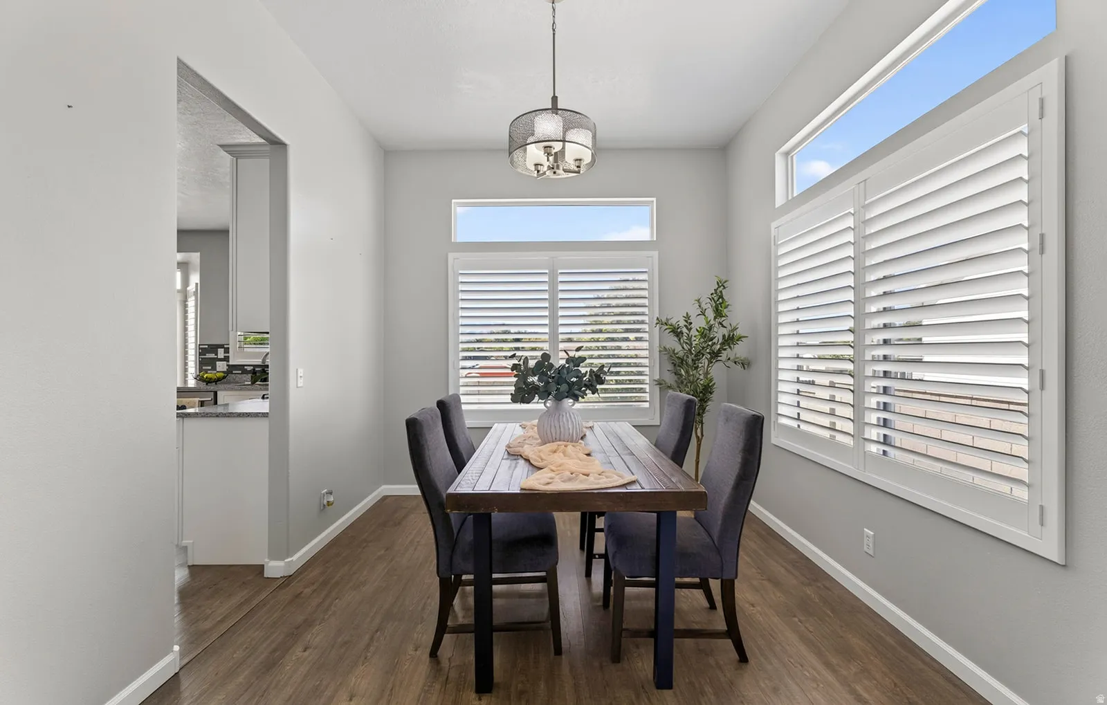 Wood-finish flooring, white plantation shutters, contemporary pendant light fixture, and a built-in transom window