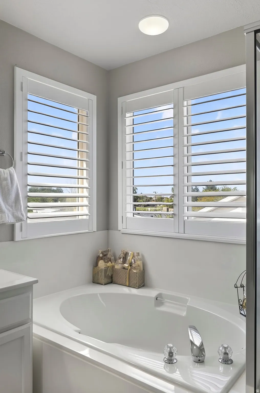 Corner soaking tub with polished chrome fixtures and multiple windows featuring white plantation shutters