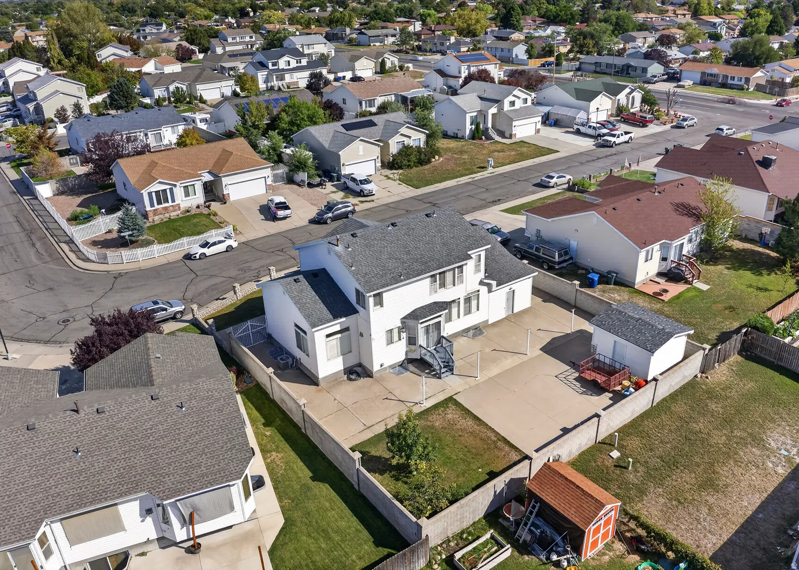 Two-story residential structure with a gray shingle roof, concrete patio, and a detached shed