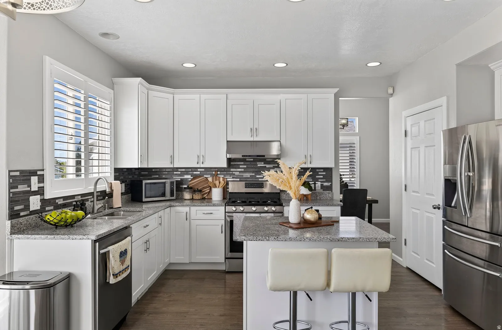 White cabinetry with stainless steel appliances, granite countertops, and a tile backsplash