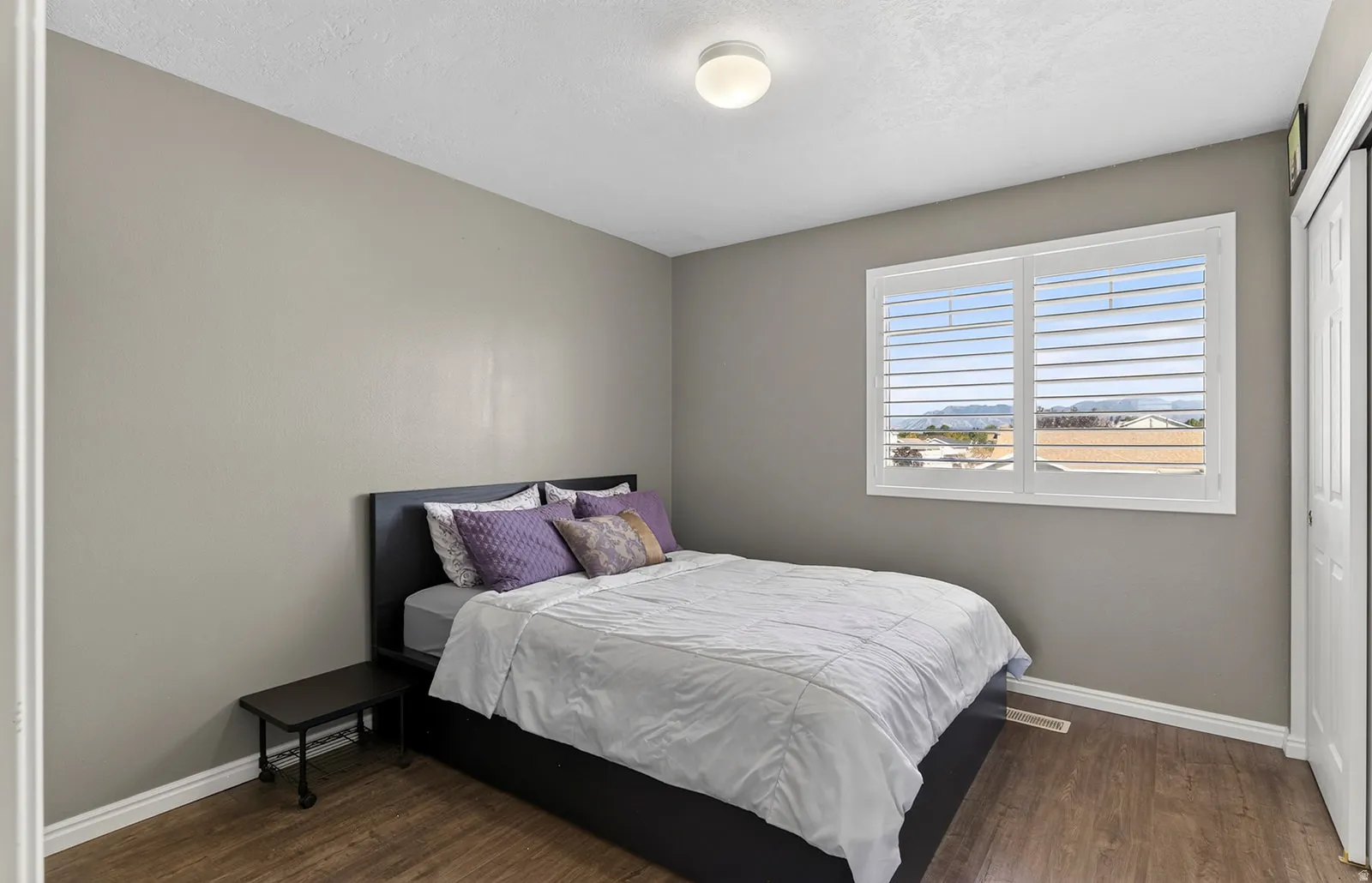 Wood-finish flooring, white baseboards, window with white plantation shutters, white door, and a flush-mount ceiling light