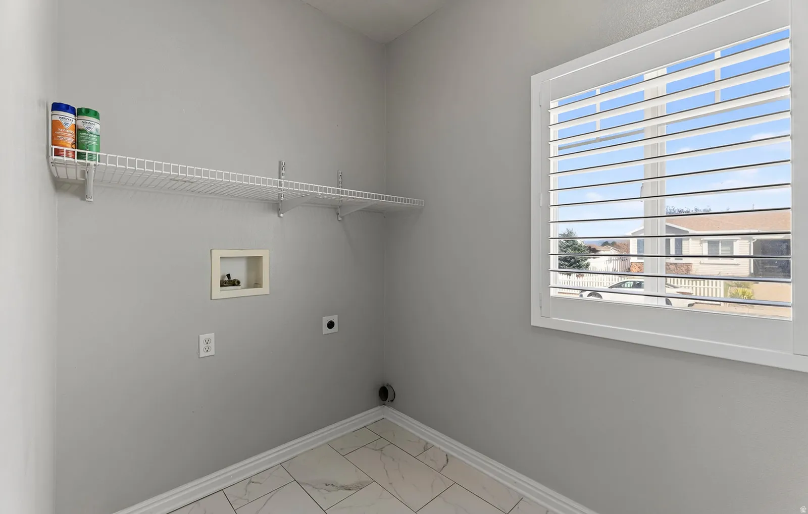 Utility room with tile flooring, wall-mounted wire shelving, and a window with white louvered shutters