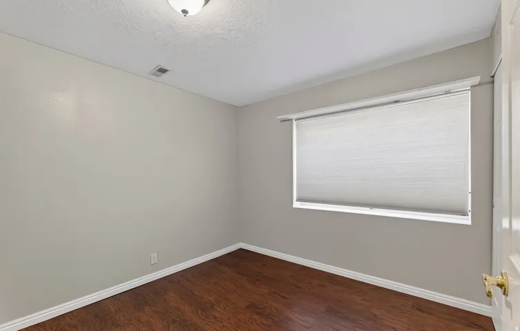 Wood-finish flooring with white baseboards, neutral wall paint, and a window featuring a roller shade