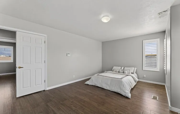 Wood-finish flooring, neutral gray wall tones, window with white louvered shutters, and a white six-panel door