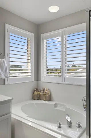 Corner soaking tub with polished chrome fixtures and multiple windows featuring white plantation shutters