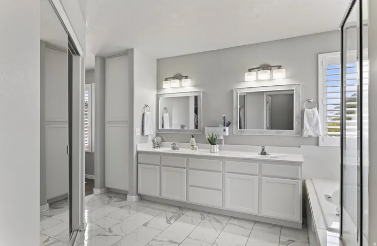 Dual vanity with white cabinetry and integrated sinks, complemented by framed mirrors and sconce lighting