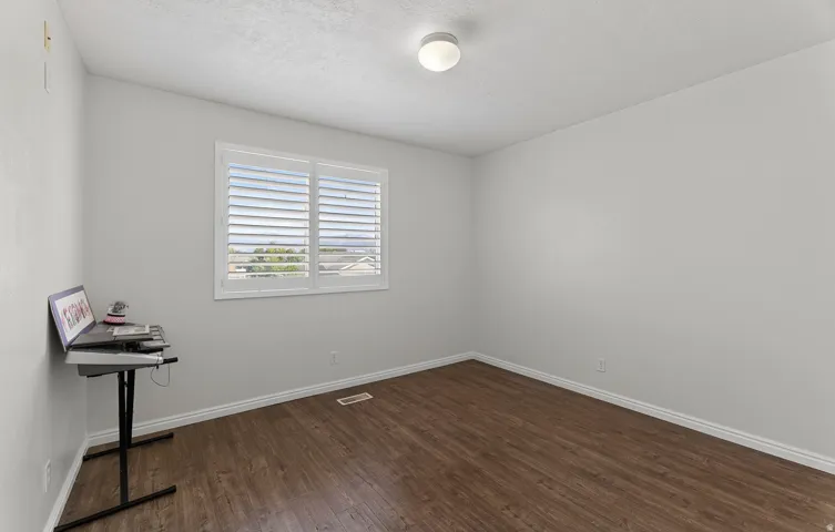 Wood-finish flooring, white walls, and a window with white plantation shutters