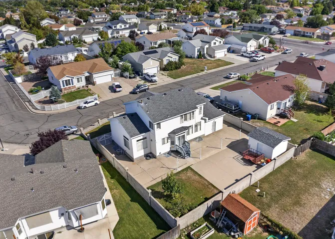 Two-story residential structure with a gray shingle roof, concrete patio, and a detached shed