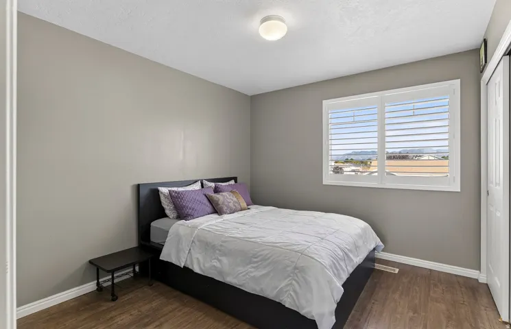 Wood-finish flooring, white baseboards, window with white plantation shutters, white door, and a flush-mount ceiling light