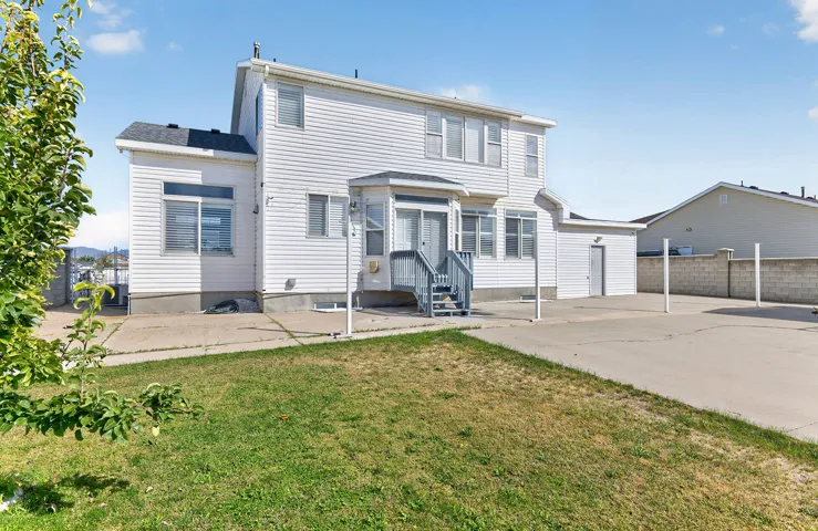 Two-story residence featuring white siding, a rear deck with stairs, a detached storage structure, and a concrete patio area