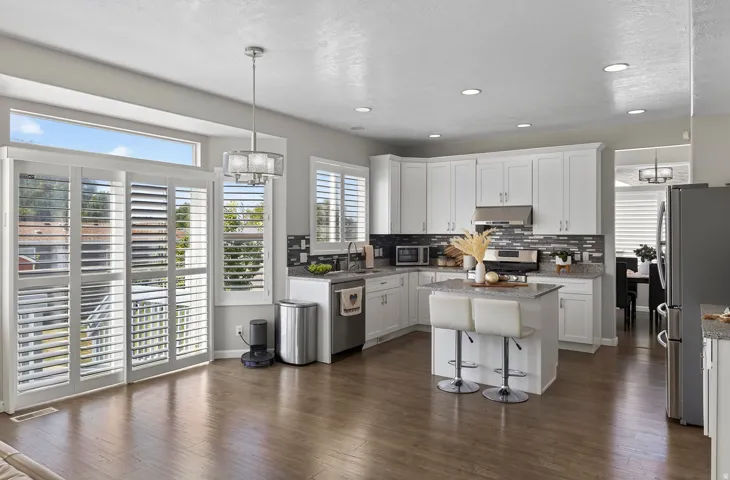 Wood-finish flooring, white cabinetry, stainless steel appliances, central kitchen island, and recessed lighting