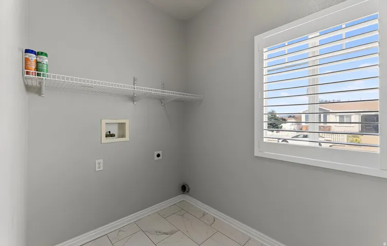 Utility room with tile flooring, wall-mounted wire shelving, and a window with white louvered shutters
