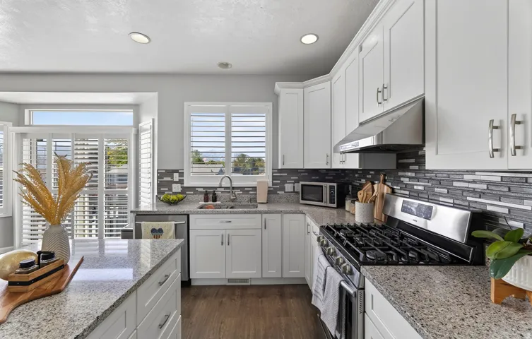 White cabinetry, granite countertops, stainless steel appliances, mosaic tile backsplash, and wood-finish flooring