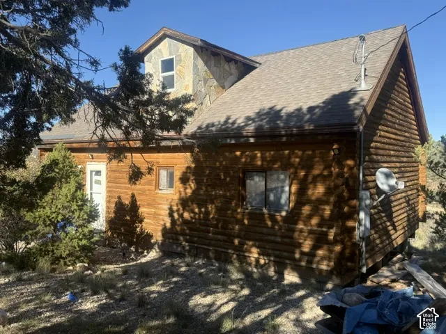 Log cabin exterior featuring horizontal log siding, stone masonry accents on the dormer, and a pitched asphalt shingle roof