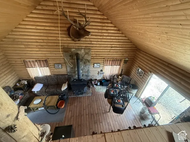 Wood-paneled interior with exposed log walls, wood-finish flooring, stone-clad fireplace with wood-burning stove, and vaulted ceiling