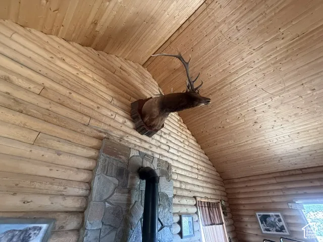 Vaulted wood-paneled ceiling, exposed log wall construction, stone-clad fireplace surround, and a visible stovepipe