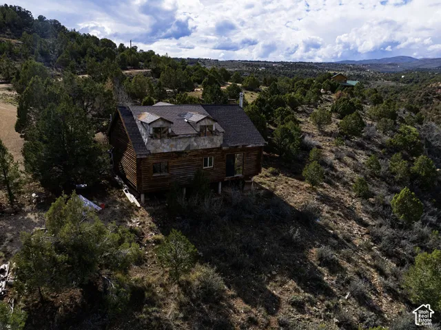 Log cabin exterior with an elevated foundation, featuring multiple dormer windows and a natural, treed landscape