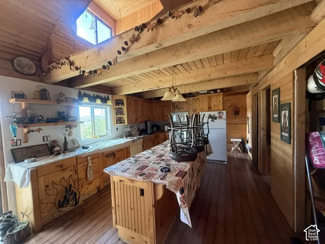Exposed wood beam ceiling, wood-finish flooring, wood cabinetry, built-in shelving, and a prominent kitchen island