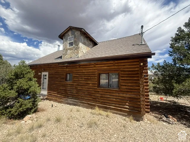 Log cabin exterior featuring a stone-clad dormer and a sloped shingle roof