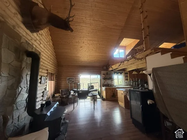 Vaulted wood-paneled ceilings, wood-finish flooring, stone-clad fireplace with wood-burning stove, and a visible loft area