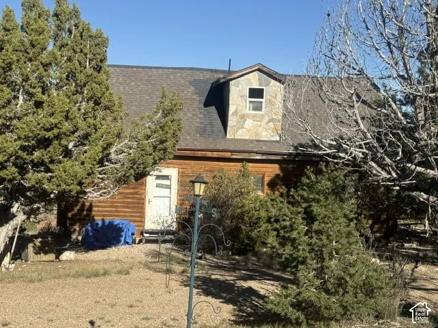 Exterior featuring wood-log siding, a roof dormer with stone cladding, and a shingled roof