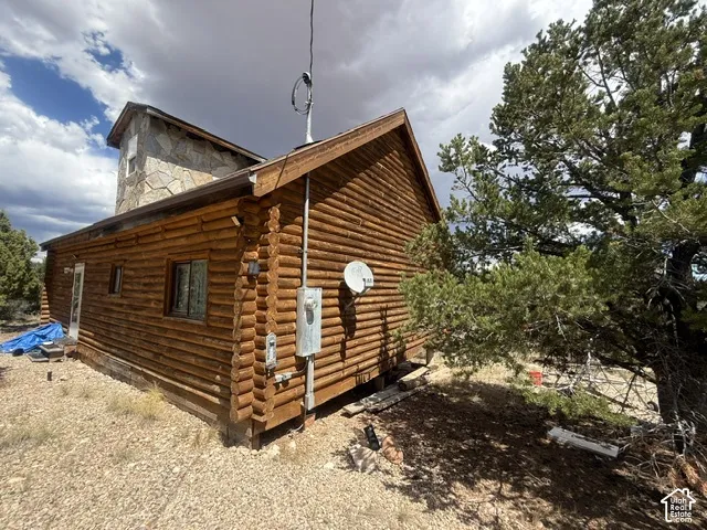 Log-style exterior with stone chimney feature, brown gutters, and a natural landscape with mature trees