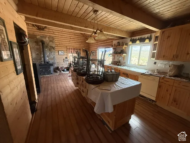 Wood-finish flooring throughout, wood-finish walls, wood-finish ceiling with exposed beams, wood-finish cabinetry, and built-in wood-burning stove with stone surround