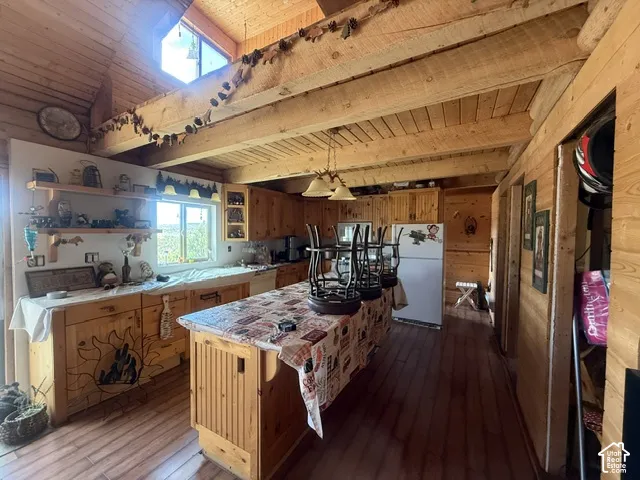 Wood-paneled walls and ceiling, exposed wood beams, wood-finish flooring, wood cabinetry, and a kitchen island with built-in storage