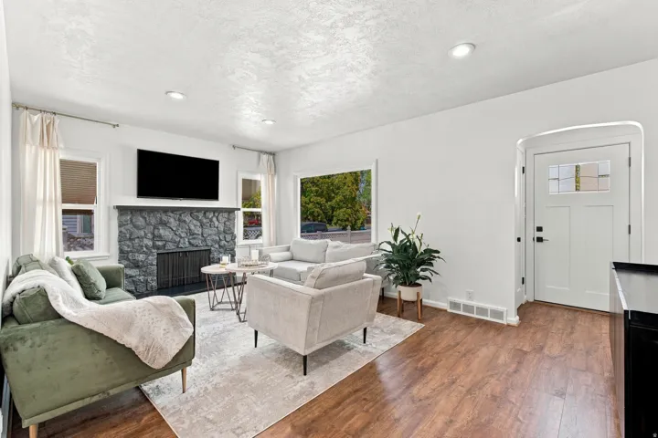 Living area featuring wood-finish flooring, a stone-clad fireplace with hearth, recessed lighting, and multiple windows
