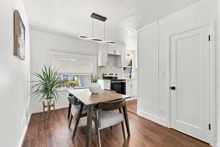 Wood-finish flooring, contemporary linear chandelier, window with horizontal blinds, white interior doors, and modern kitchen cabinetry