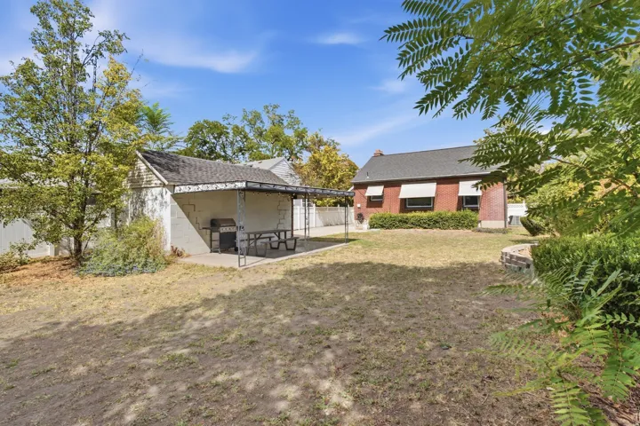 Expansive outdoor space featuring a covered patio, brick-built planter, and mature trees