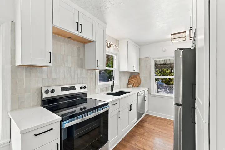 White shaker-style cabinetry with matte black hardware, light-toned tile backsplash, stainless steel range, and wood-finish flooring