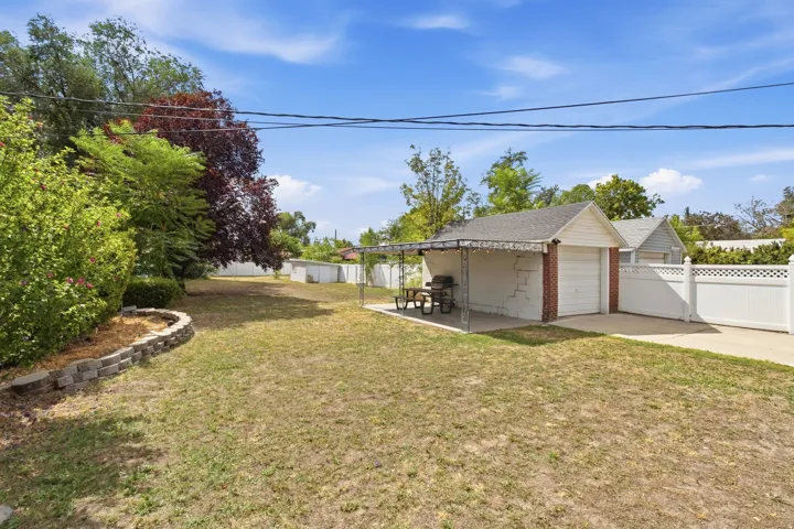 Detached garage with white panel door, red brick accents, and an attached covered patio
