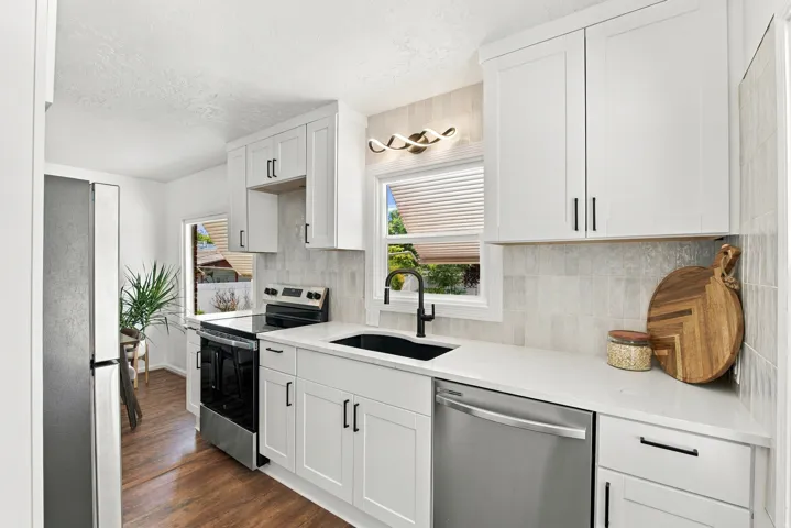 White shaker cabinetry, light-toned backsplash, stainless steel appliances, black sink, wood-finish flooring