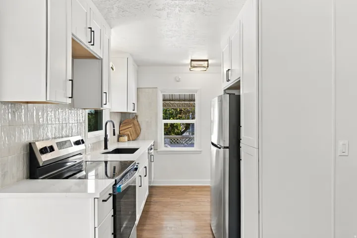 Galley kitchen featuring white cabinetry with black hardware, wood-finish flooring, white countertops, and a full suite of stainless steel appliances