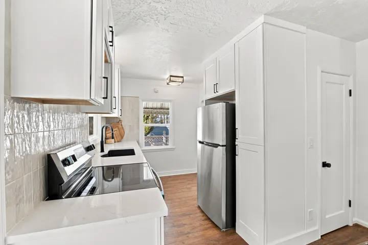 White shaker cabinetry, light-toned tile backsplash, stainless steel appliances, and wood-finish flooring