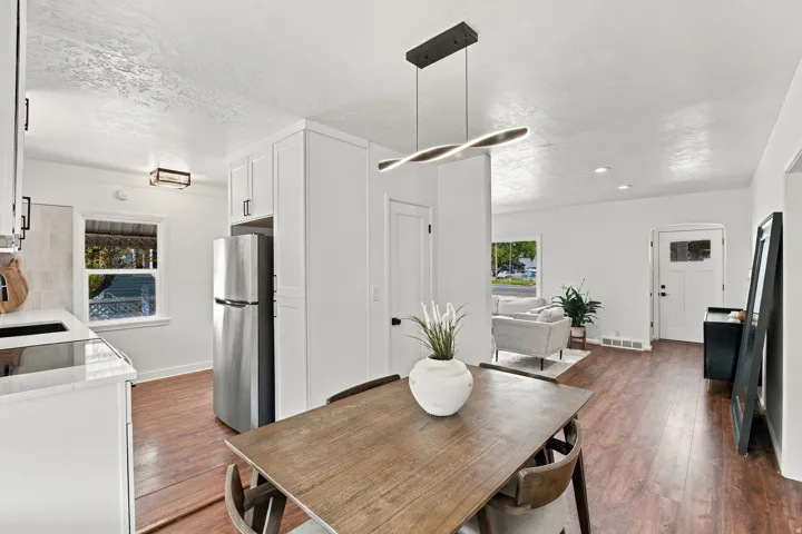 Wood-finish flooring throughout, white cabinetry with dark hardware, a stainless steel refrigerator, white countertops, and a contemporary pendant light fixture