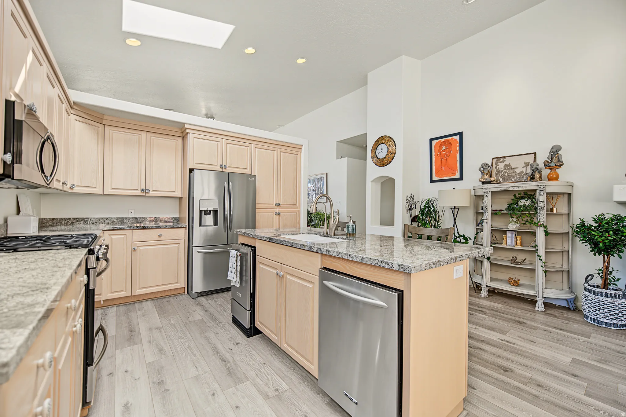 Kitchen featuring light wood cabinetry, stainless steel appliances, granite countertops, wood-finish flooring, and a skylight