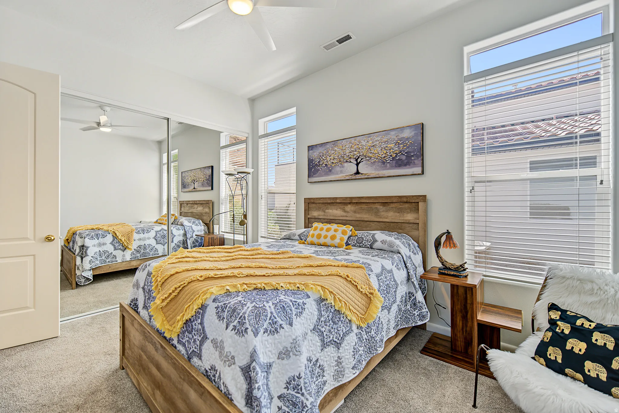 Carpeted flooring, vaulted ceiling, ceiling fan, mirrored closet doors, and large windows with blinds