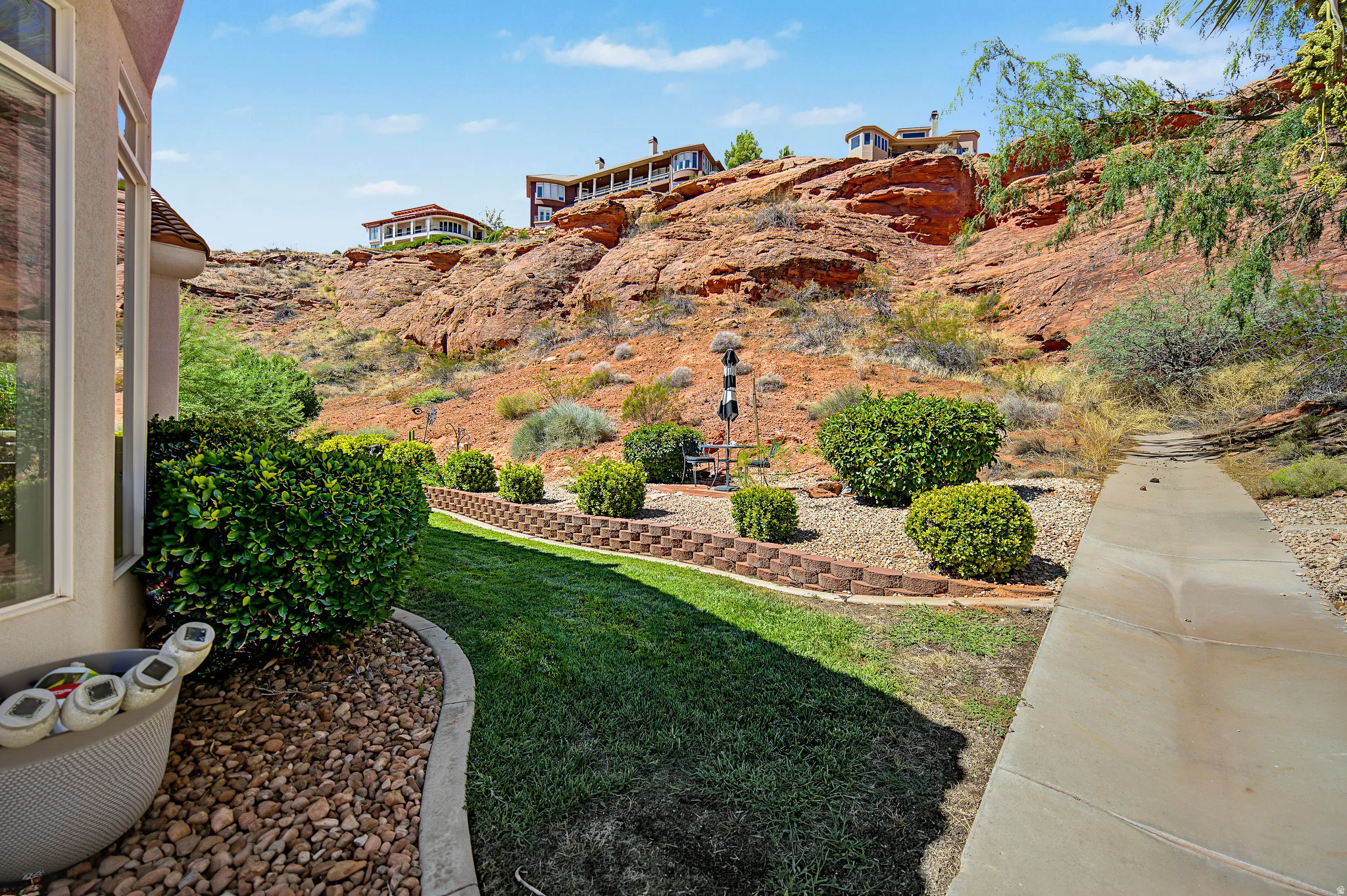 Lush green lawn with a curved concrete border, surrounded by ornamental shrubs and a retaining wall