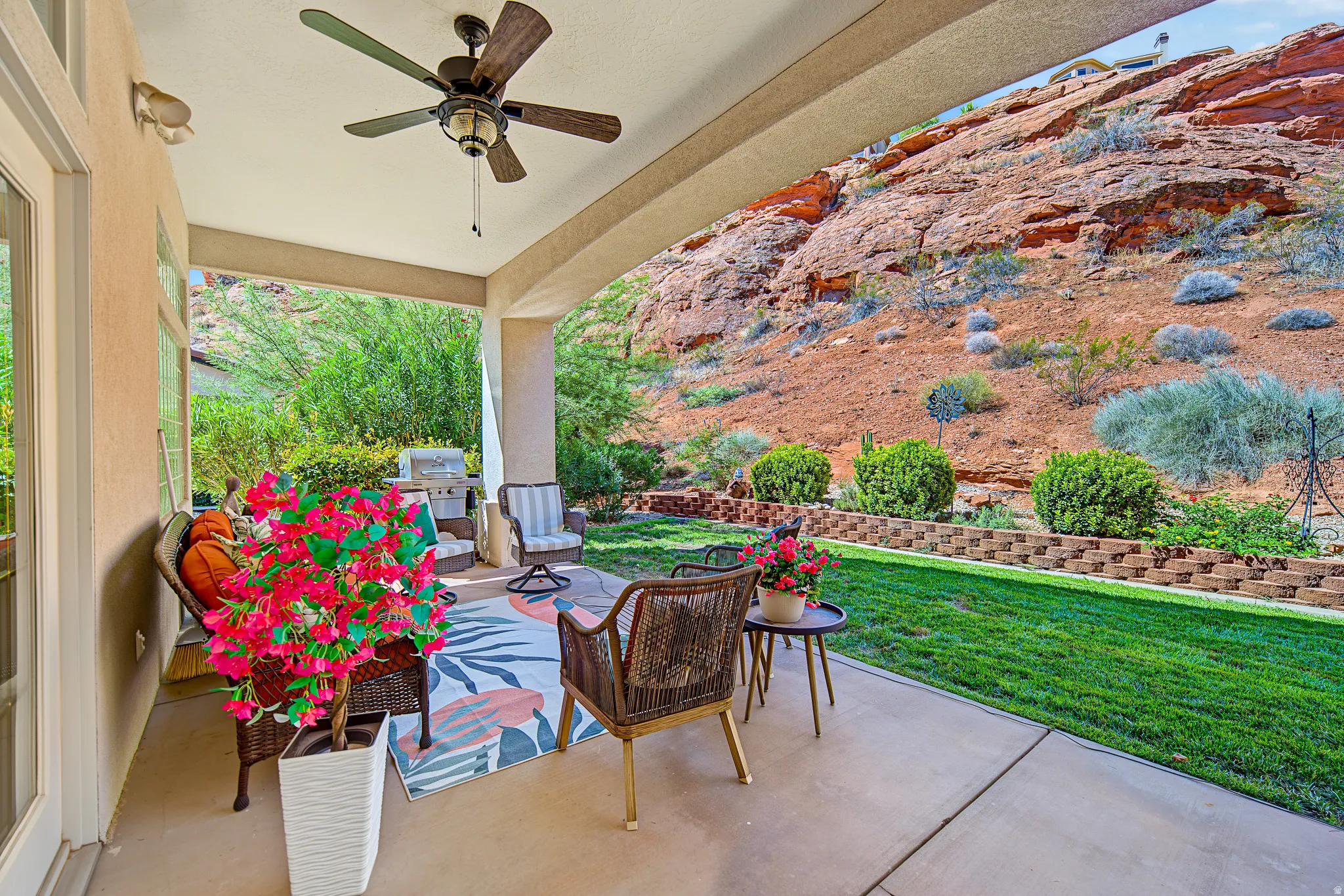 Covered patio with a ceiling fan, concrete flooring, and a stone retaining wall