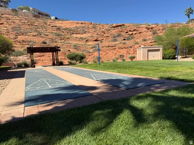 Recreational shuffleboard courts with surrounding paver patio and expansive lawn area, set against a natural rock hillside
