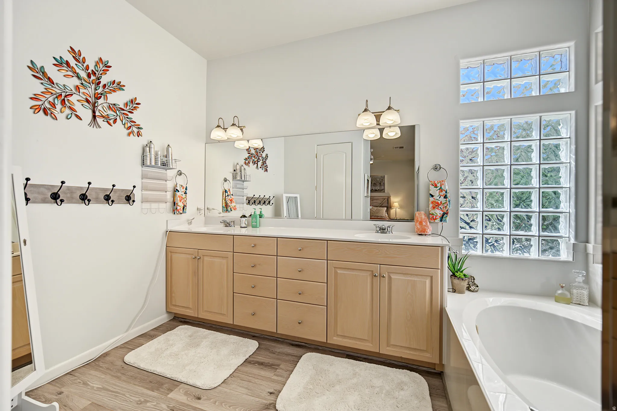 Double vanity with light wood-finish cabinetry, a large mirror, and dual light fixtures