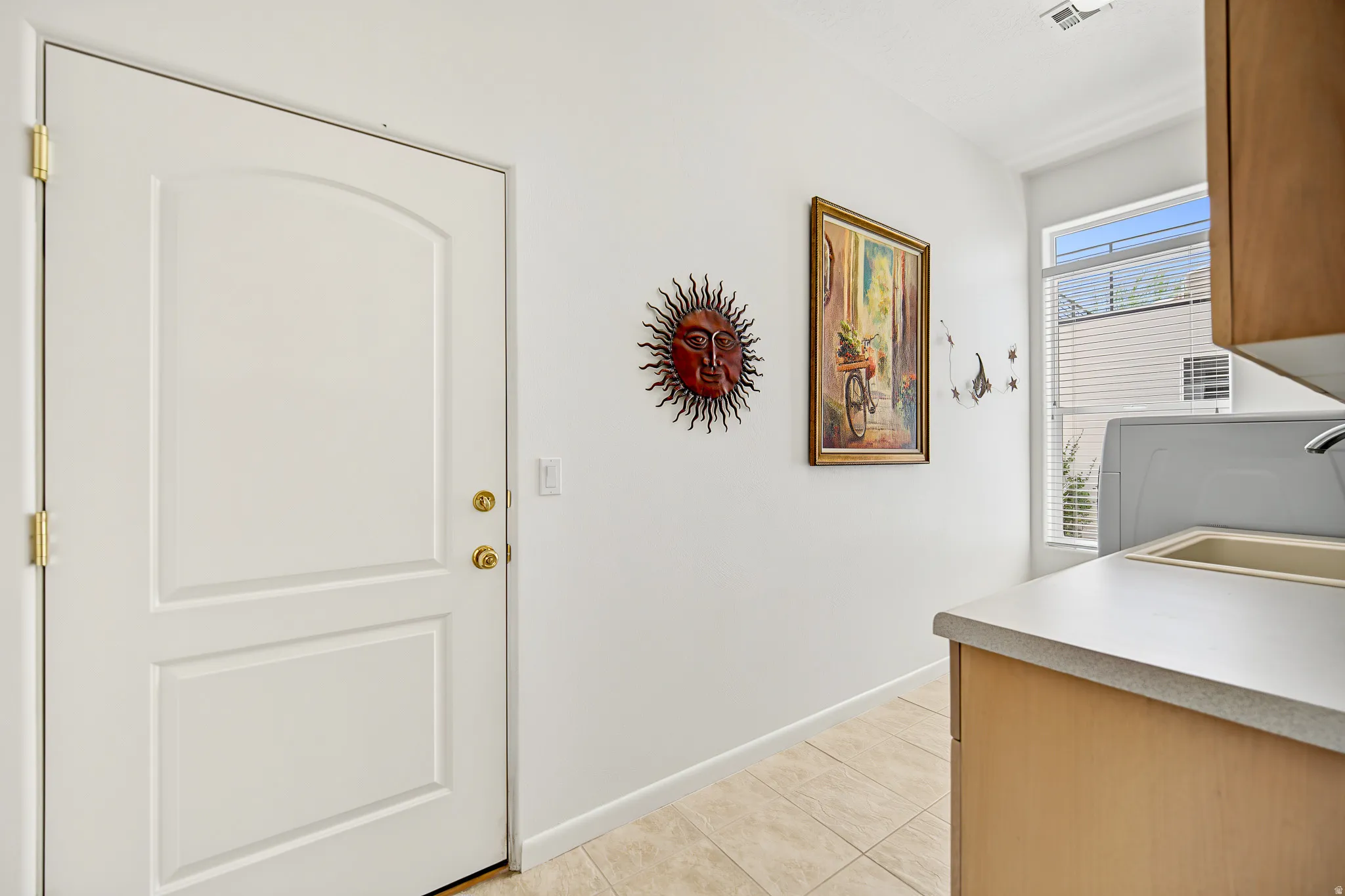 White paneled door with brass hardware, tile flooring, built-in cabinetry, and a window with horizontal blinds