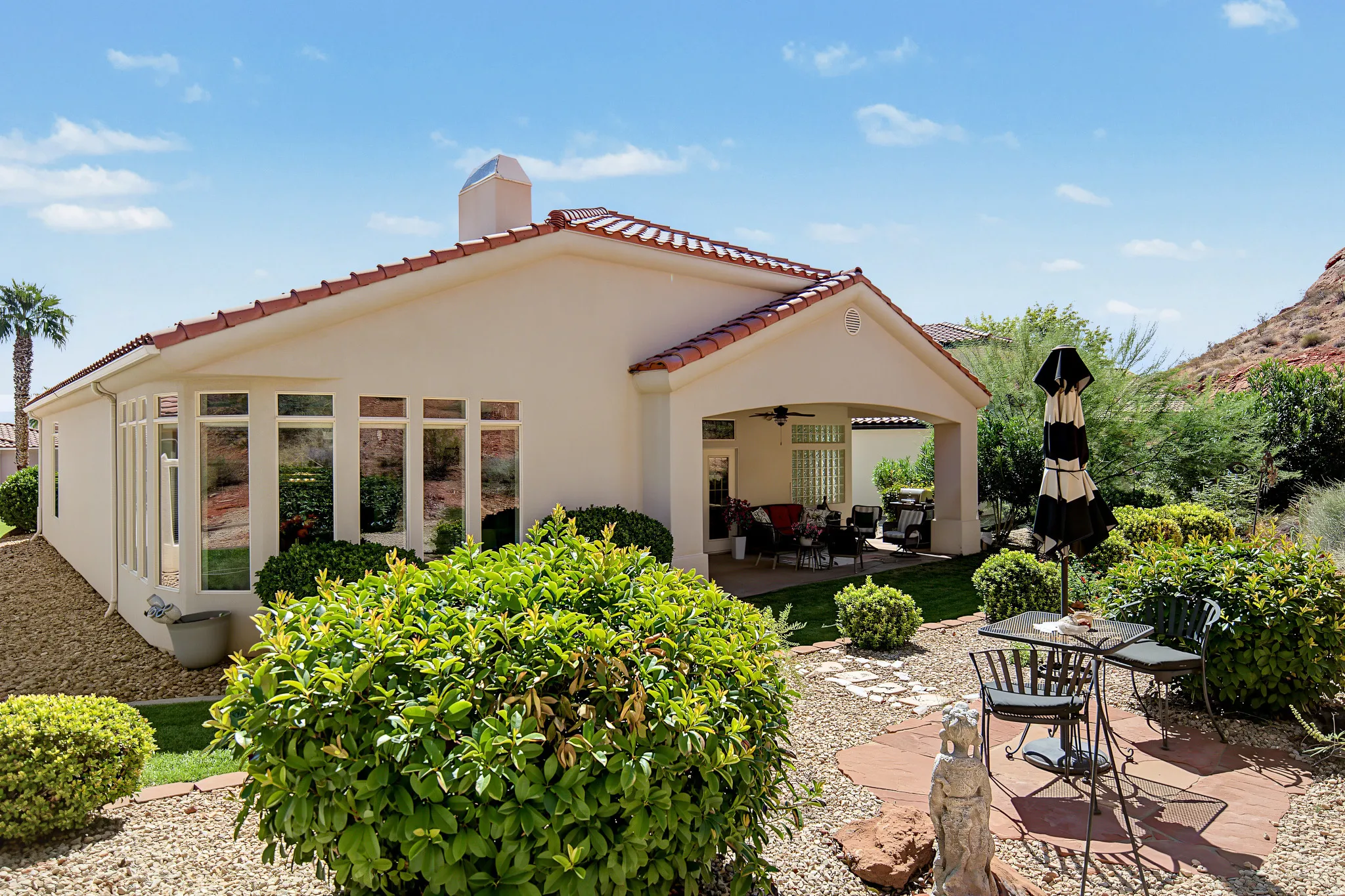 Mediterranean-style exterior with a tile roof, stucco finish, expansive windows, and a covered patio