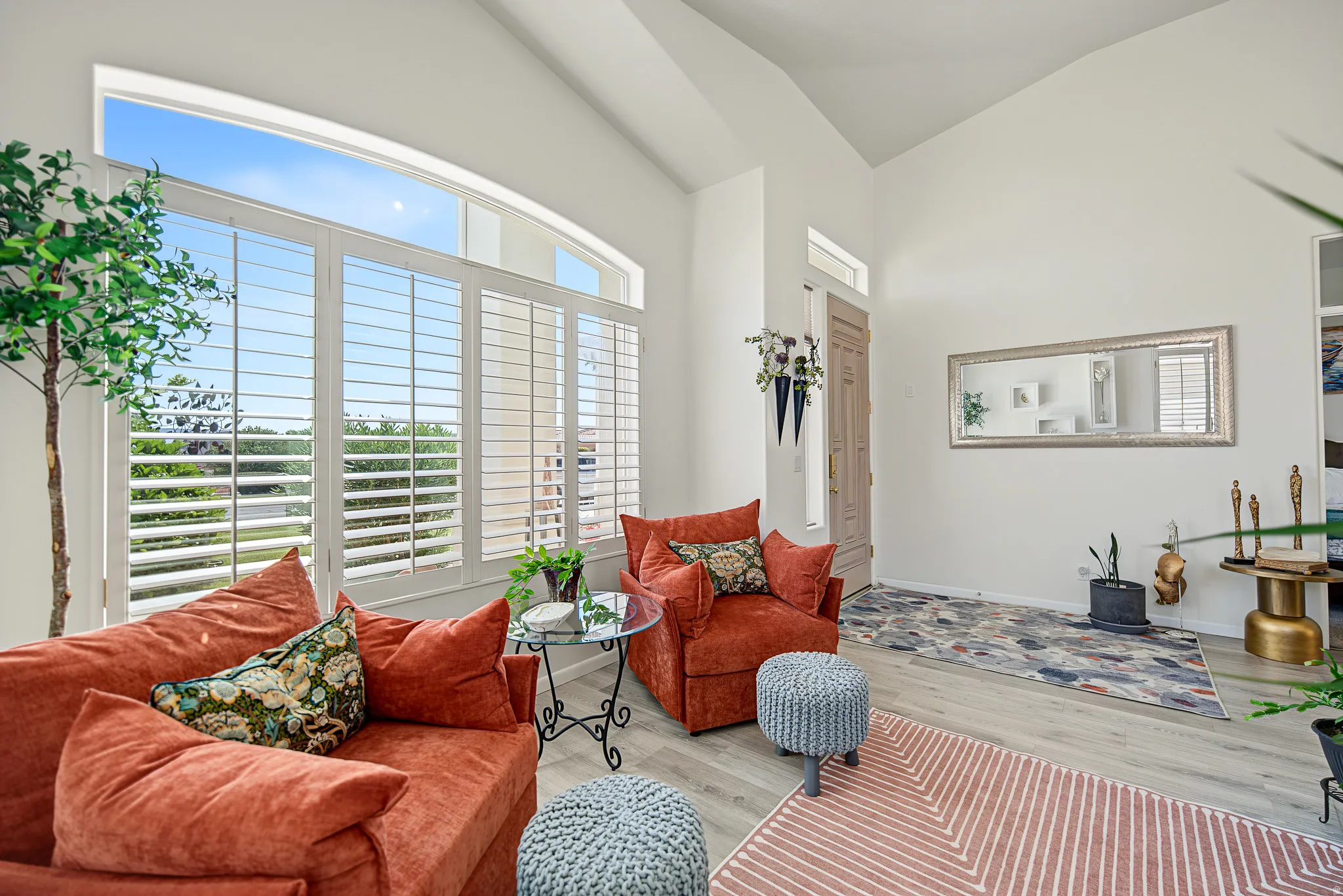 Vaulted ceilings, expansive windows with plantation shutters, light wood-finish flooring, and a neutral wall palette