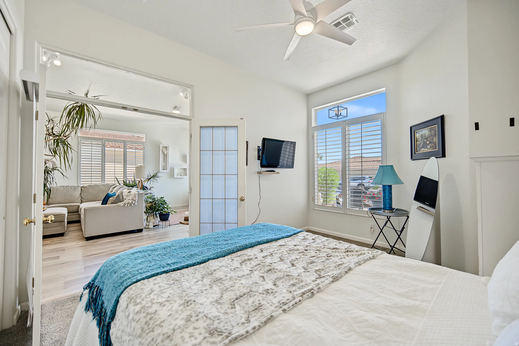 Ceiling fan with integrated lighting, window with plantation shutters, transom window, wood-finish flooring in adjacent area, and white paneled door with glass inserts