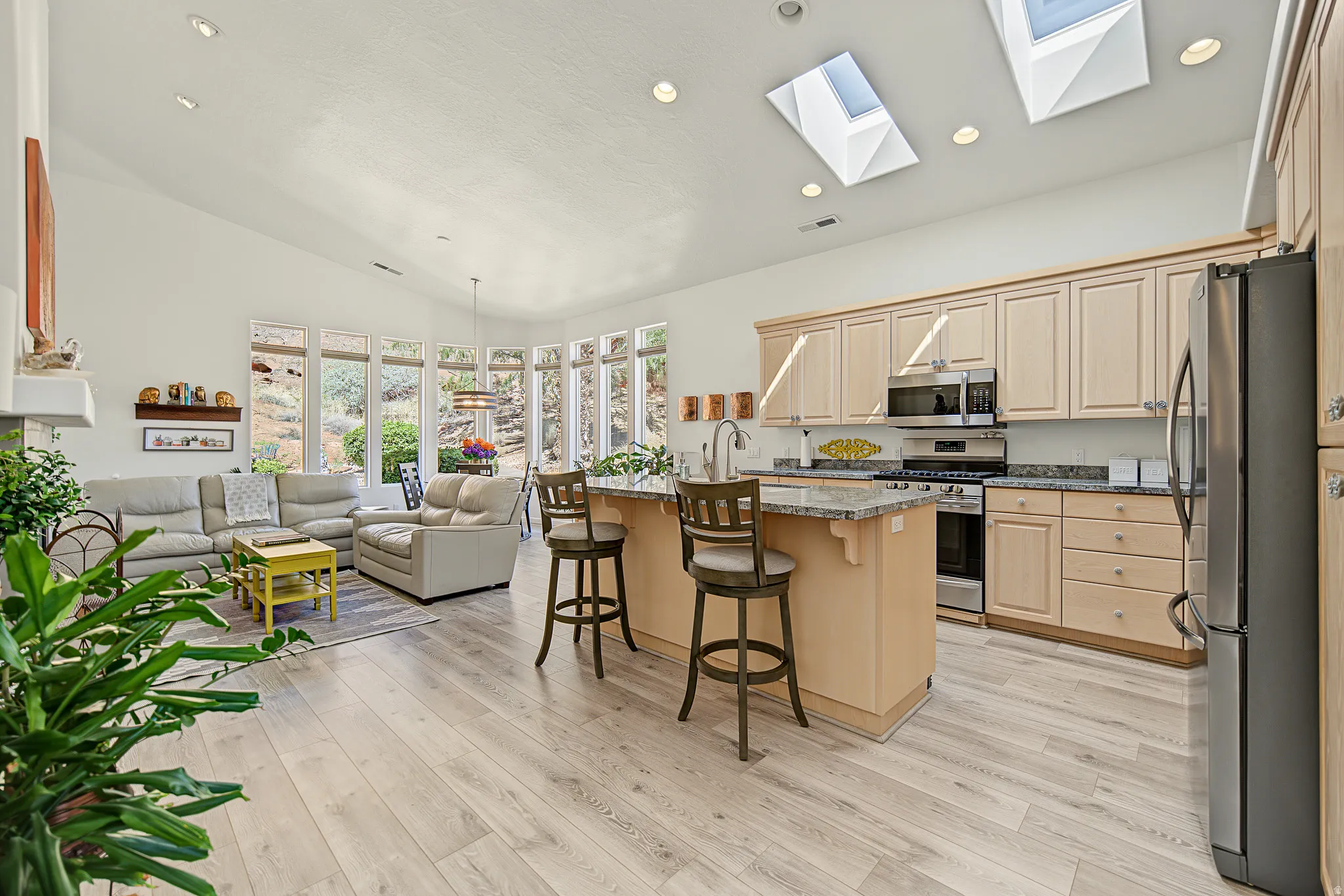 Open-concept living space with vaulted ceilings, skylights, wood-finish flooring, a kitchen island with seating, and a full wall of windows